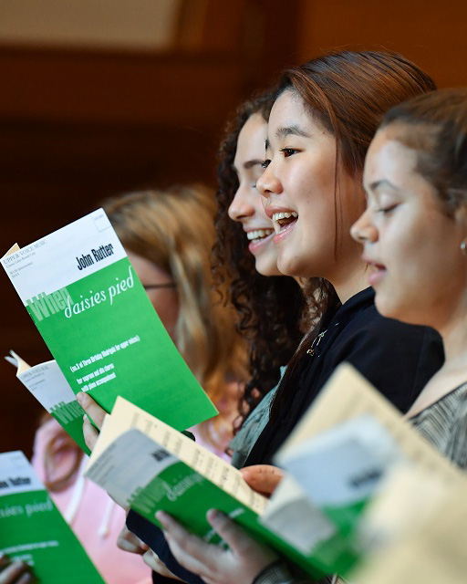 A group of young RCMJD students, singing, holding green music books.